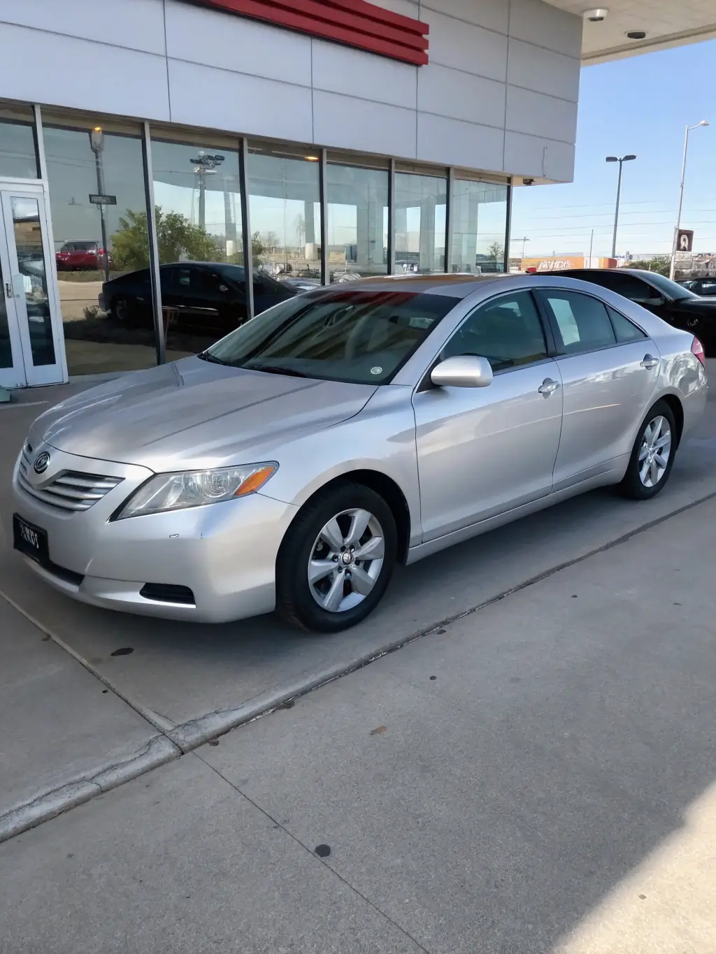 A sleek, silver sedan parked in front of a modern car dealership, showcasing its elegant design and appeal to potential buyers.